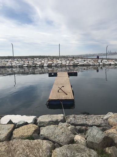 A vertical shot of a small wooden dock on the sea surrounded by rocks under a cloudy sky