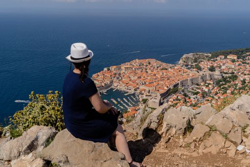 A high angle shot of a female sitting on the rock in Dubrovnik, Croatia near the sea