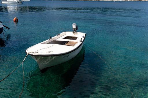 A small white boat tied on the shore of a lake