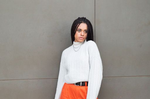 An attractive Afro-American woman with dreads wearing bright orange pants and a sweater
