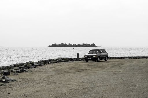 car in the middle of nowhere in front of the beach with a mountain in the background