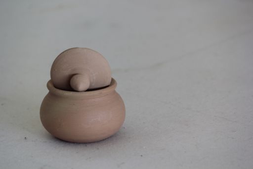 A closeup shot of a clay pot with a lid on  a gray background