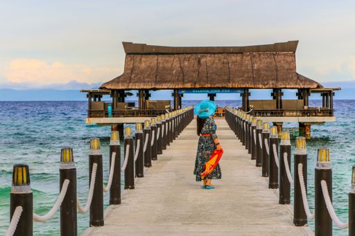 A view of a female standing on a pier leading to a wooden dock  on the ocean