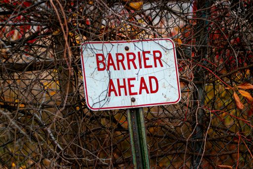 A selective focus shot of a barrier ahead sign leaned against a metal fence