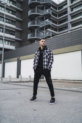 A vertical shot of a stylish guy wearing a plaid jacket, a black hoodie, black pants, and sneakers