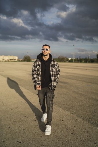 A stylish cool Caucasian male with sunglasses walking on a road in background of gloomy clouds