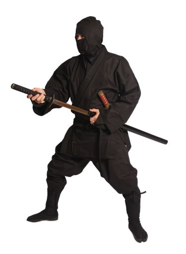 A young man dressed in a traditional Japanese ninja costume, holding a sword in his hands, stands against a white studio background