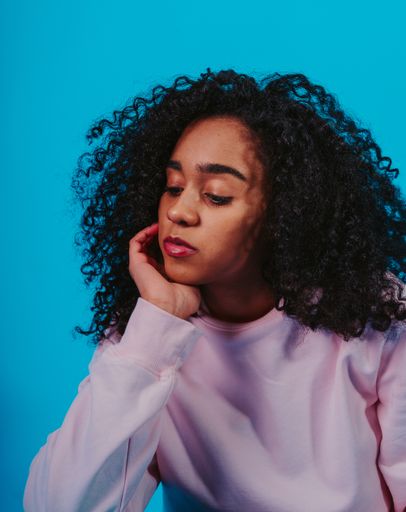 A portrait of a young Hispanic female with curly hair sitting against a blue background