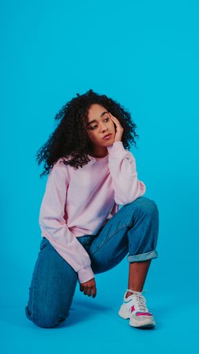 A beautiful curly haired girl posing in a pink sweater and jeans on a blue background