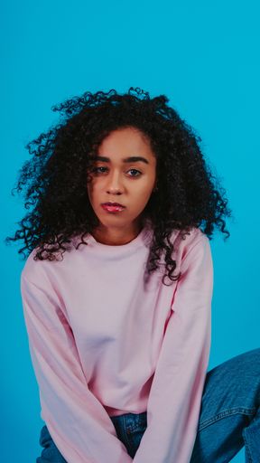 A beautiful curly haired girl posing in a pink sweater and jeans on a blue background