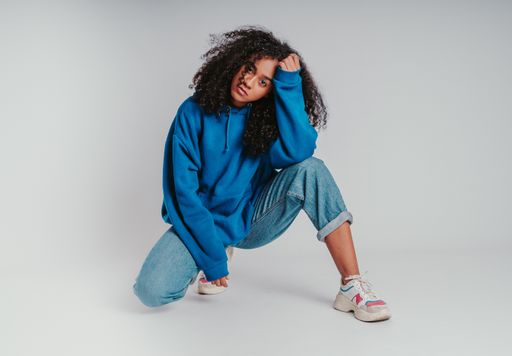A beautiful curly-haired girl posing in a blue sweater and jeans on a white background