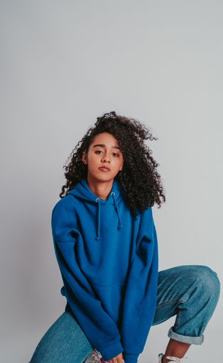 A beautiful curly-haired girl posing in a blue sweater and jeans on a white background