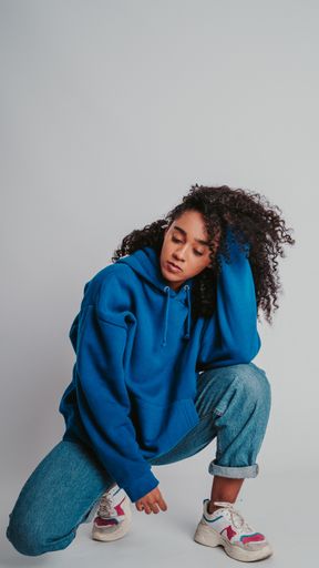 A beautiful curly-haired girl posing in a blue sweater and jeans on a white background