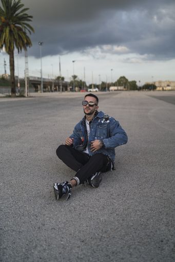 A vertical shot of a stylish handsome guy wearing sunglasses sitting on the stre