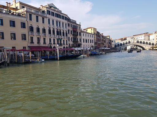 A beautiful shot boats on the water in the middle of buildings with a bridge in the distance in Italy
