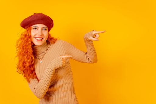 A red-haired Caucasian woman in a beret pointing on the right, on a yellow background, with copy space