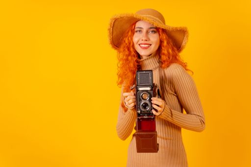A red-haired Caucasian tourist with a hat and vintage camera on a yellow background, with copy space