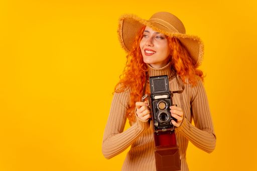 A red-haired Caucasian tourist with a hat and vintage camera on a yellow background, with copy space