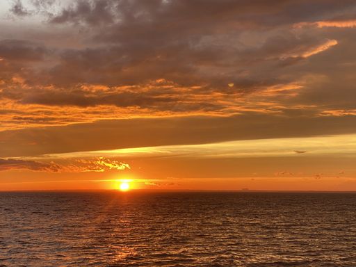 A majestic view of a setting down sunset sun with a reflection on a calm seawater surface
