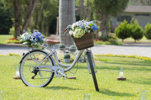 A closeup of a bicycle with flower bouquets in the front basket and the back, on the green grass during daylight