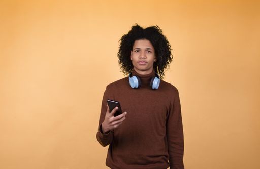 shot of a young African American man with headphones holding a cell phone