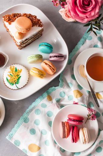 A top view of macarons and cakes with a cup of tea next to fresh flowers