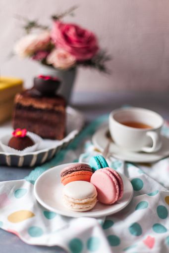 A selective focus of macarons on blurred background of a cup of tea next to fresh flowers