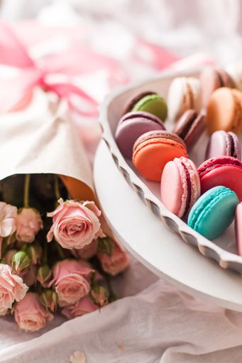 A vertical selective focus of colorful macarons next to delicate rose bouquet