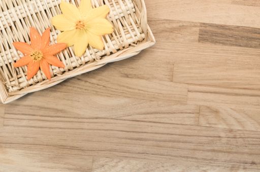 A top view closeup of two orange and yellow artificial flowers on a thatched basket on a wooden table