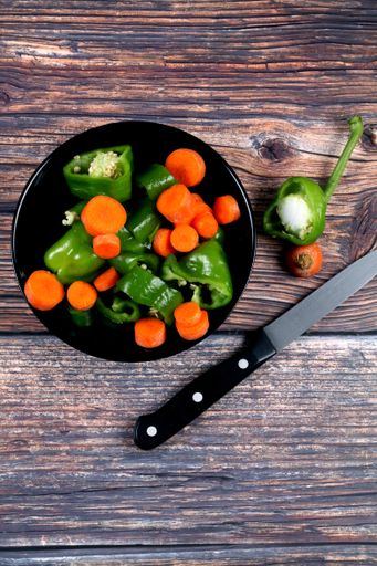 A vertical shot of a salad with carrots and green peppers in a bowl on a wooden table with a knife