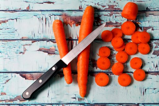 A closeup shot of a knife on carrots and chopped carrots on a wooden surface