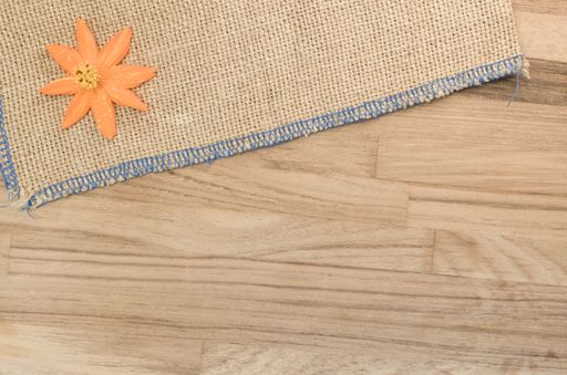 A top view closeup of an orange artificial flower on a thatched basket on a wooden table