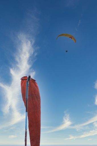 A low angle shot of a paraglider flies in the sky against the background of the windsock cone