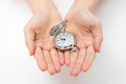 A closeup shot of hands holding a silver pocket watch on a white background