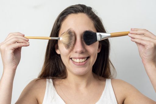 A closeup shot of a cheerful young lady closing her eyes with different makeup brushes