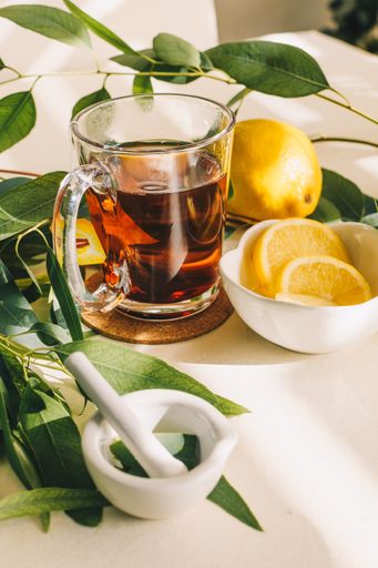 A vertical shot of a cup of herbal tea with lemon and eucalyptus leaves in a small ceramic mortar