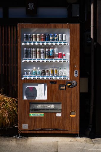 A white snack machine standing in front of a brick building in an urban street