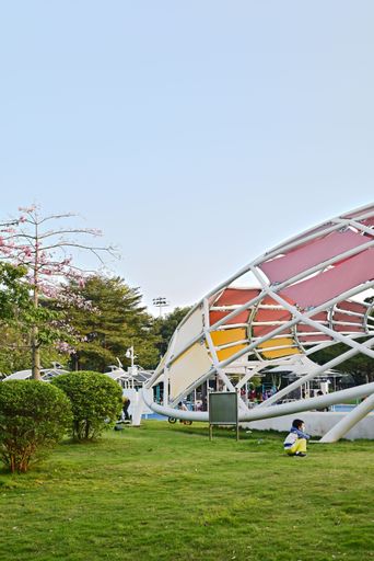 A vertical shot of a children's playground and a kid sitting on the grass and looking forward