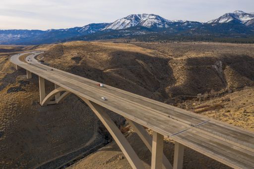 A freeway route crosses an arch span bridge in a scenic mountainous landscape.
