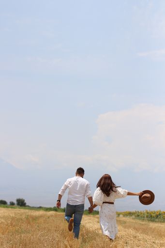A vertical shot of a happy young couple running in a dry grass field on background of the sky