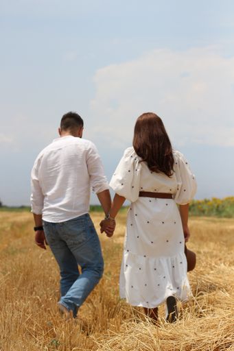 A vertical shot of a happy young couple walking in a dry grass field on background of the sky