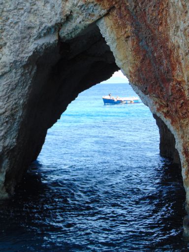 A vertical shot of a natural rock arch in a sea and a boat sailing nearby in Zakynthos island, Greece