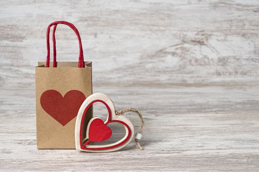 A gift paper bag with a heart and heart-shaped wooden decor on the wooden background with copy space