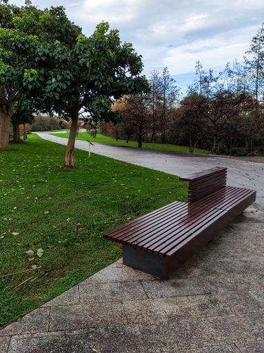A vertical shot of a llamas park in Santander, Spain with an empty wooden bench and curvy walkway