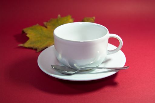 A teacup with an autumn maple tree leaf on a red background