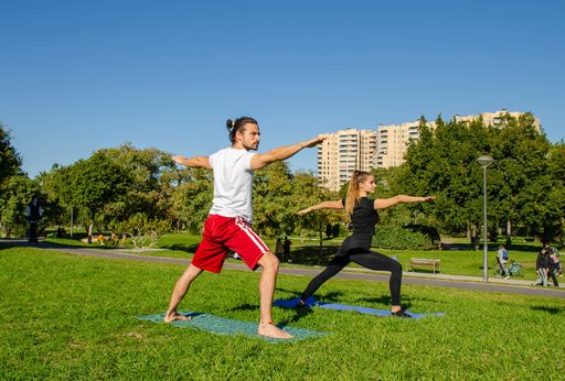 A beautiful sporty Caucasian couple in a protective face mask doing yoga outdoors in a public park