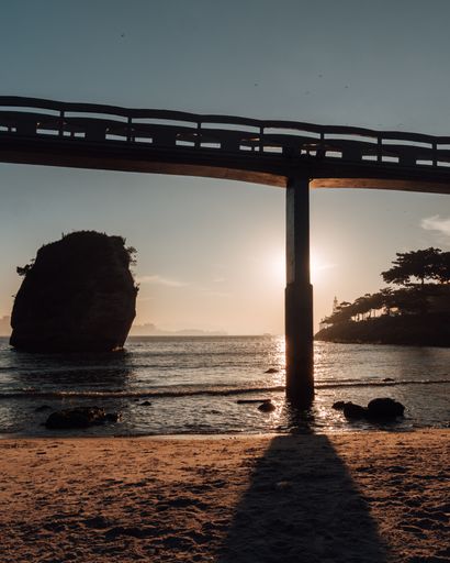 A bridge over the seashore hiding the sinking golden sun