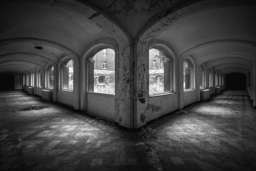 A grayscale shot of the hallways of an abandoned building with broken windows - great for horror concepts