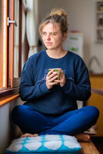 A vertical shot of a young Caucasian blonde woman drinking tea near the window