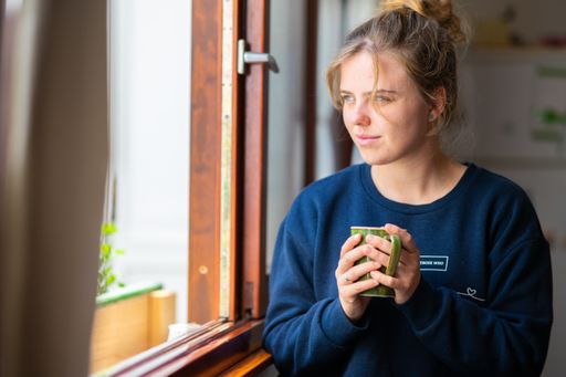 A young Caucasian blonde woman drinking tea near the window